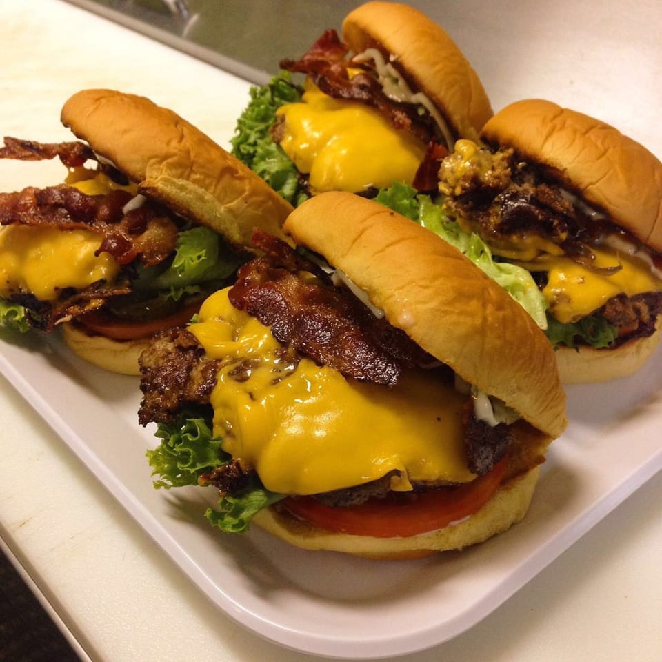 Four bacon cheeseburgers with melted cheese, lettuce, and tomato on a white platter.
