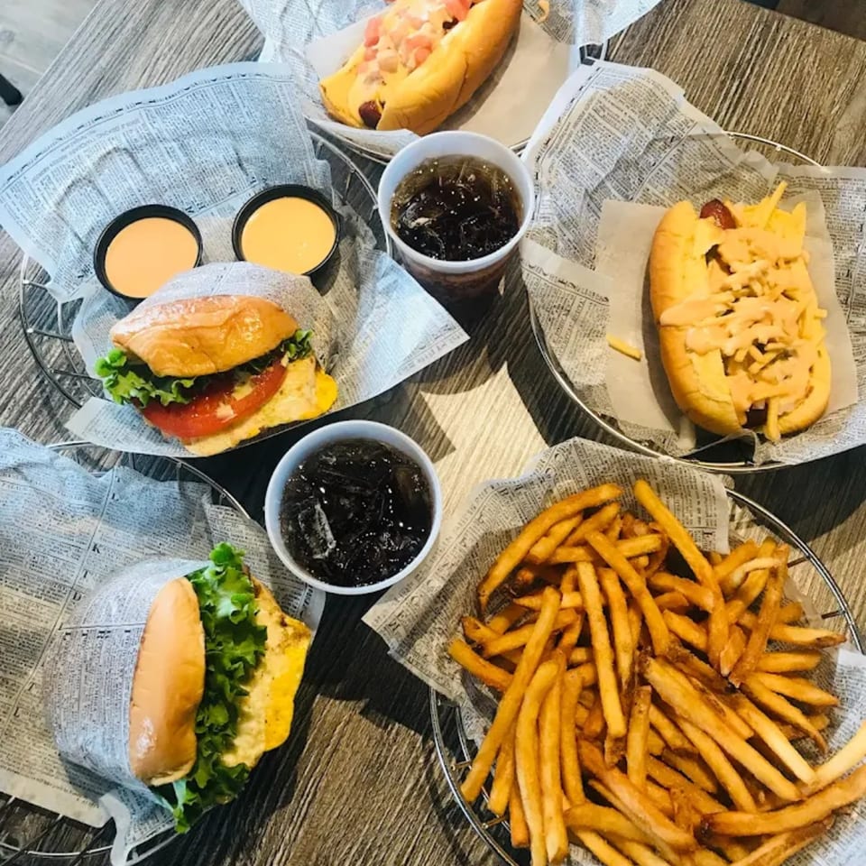 Burgers, hot dogs, fries, and sodas served in baskets lined with newspaper on a wooden table.