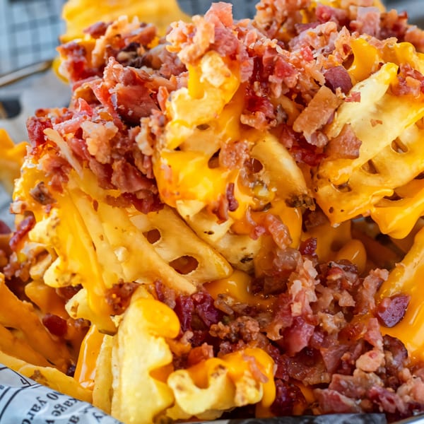 Close-up of Burbowl's waffle fries smothered in melted cheese and crispy bacon bits.