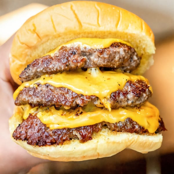 Close-up of a triple cheeseburger from Burbowl, featuring three patties and melted cheese.